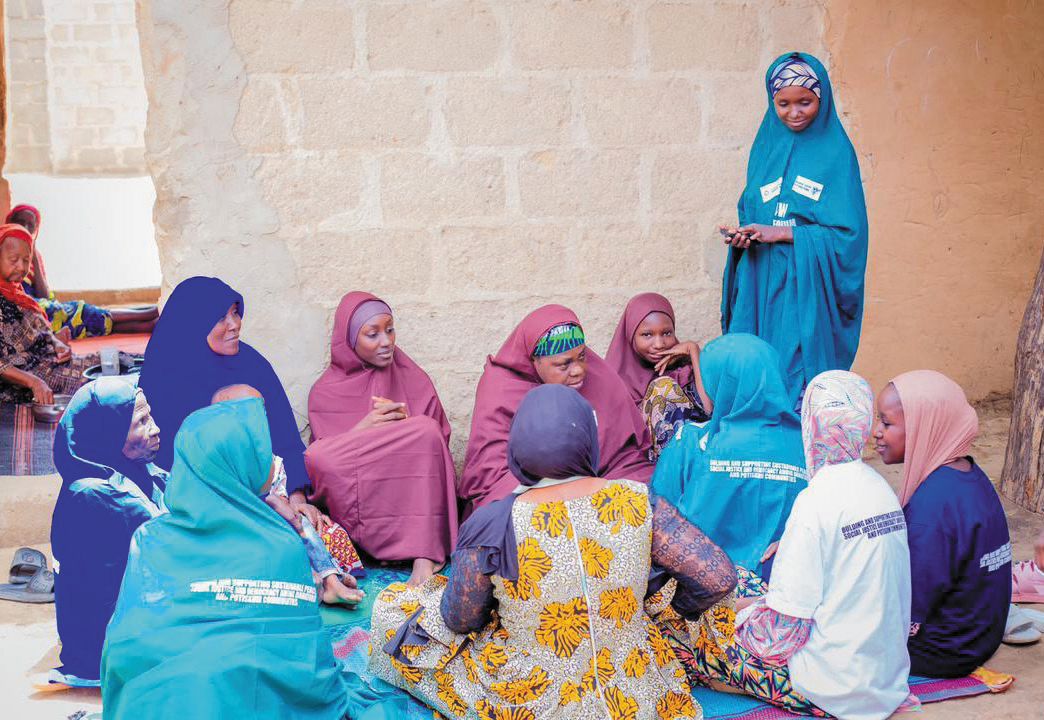A ZAIDF facilitator in blue speaks with women seated in a circle during a community session