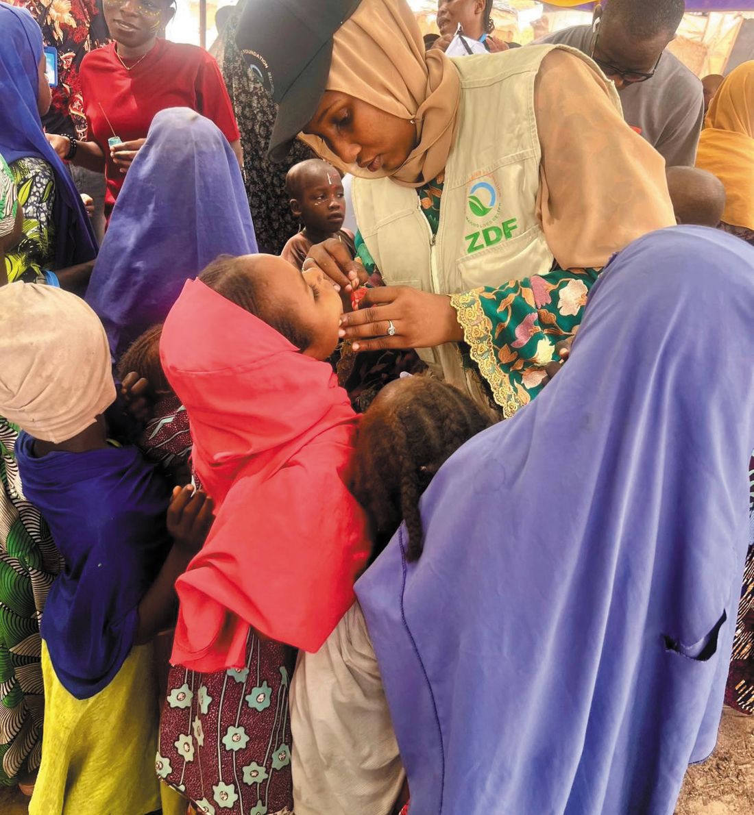 A ZAIDF team member in a ZDF vest comforts a child among displaced families at Elmaskin Camp