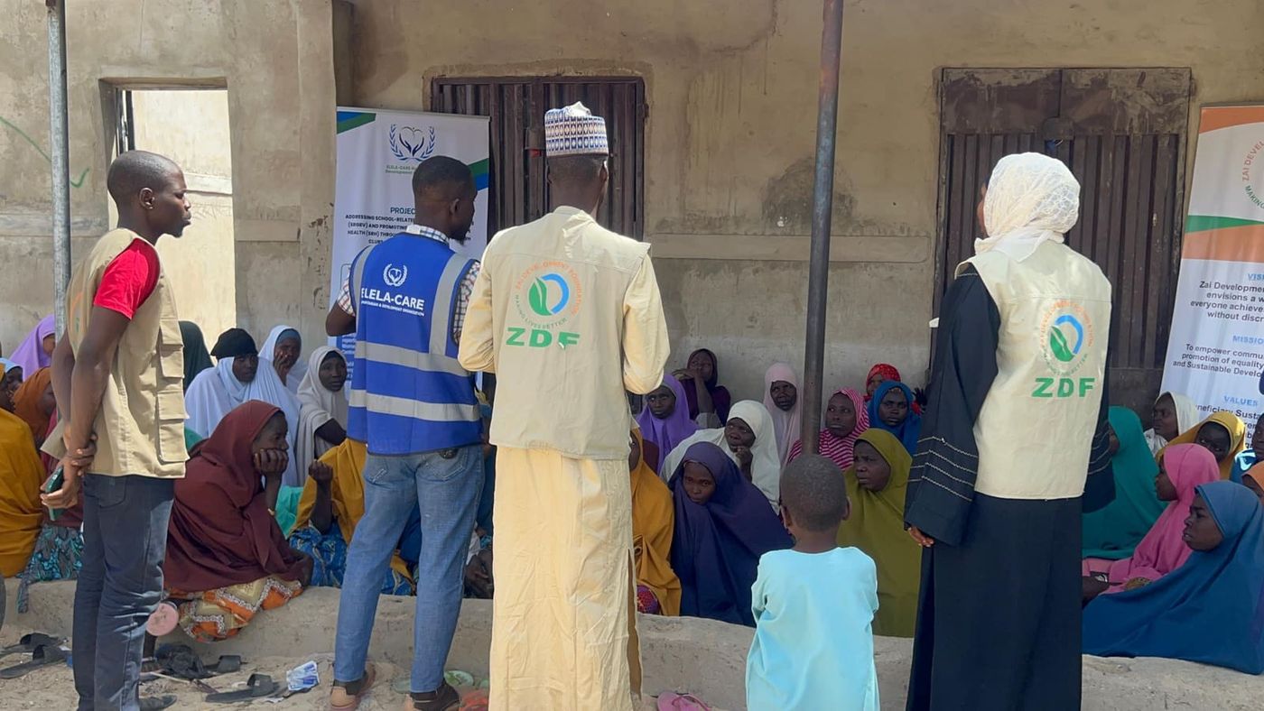 ZAIDF field team members in ZDF vests meet women and children seated outdoors