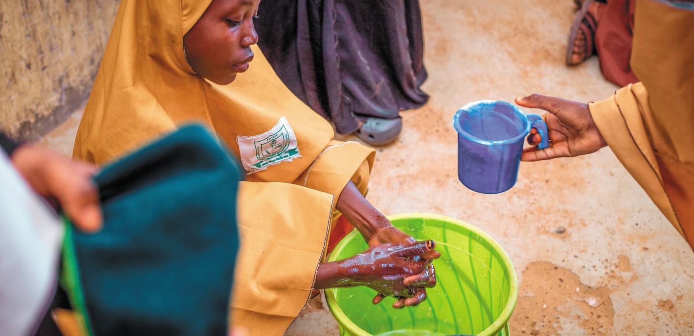 A girl washes her hands from a cup poured over a green basin