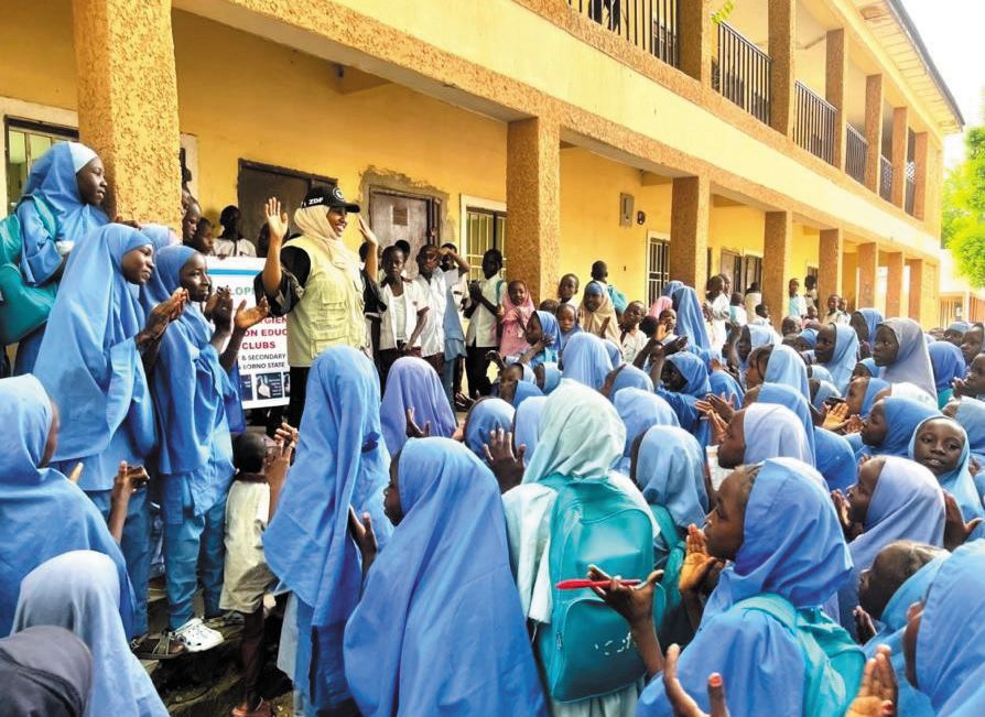 Pupils in blue headscarves gather outside a school building for a CHASE Club session