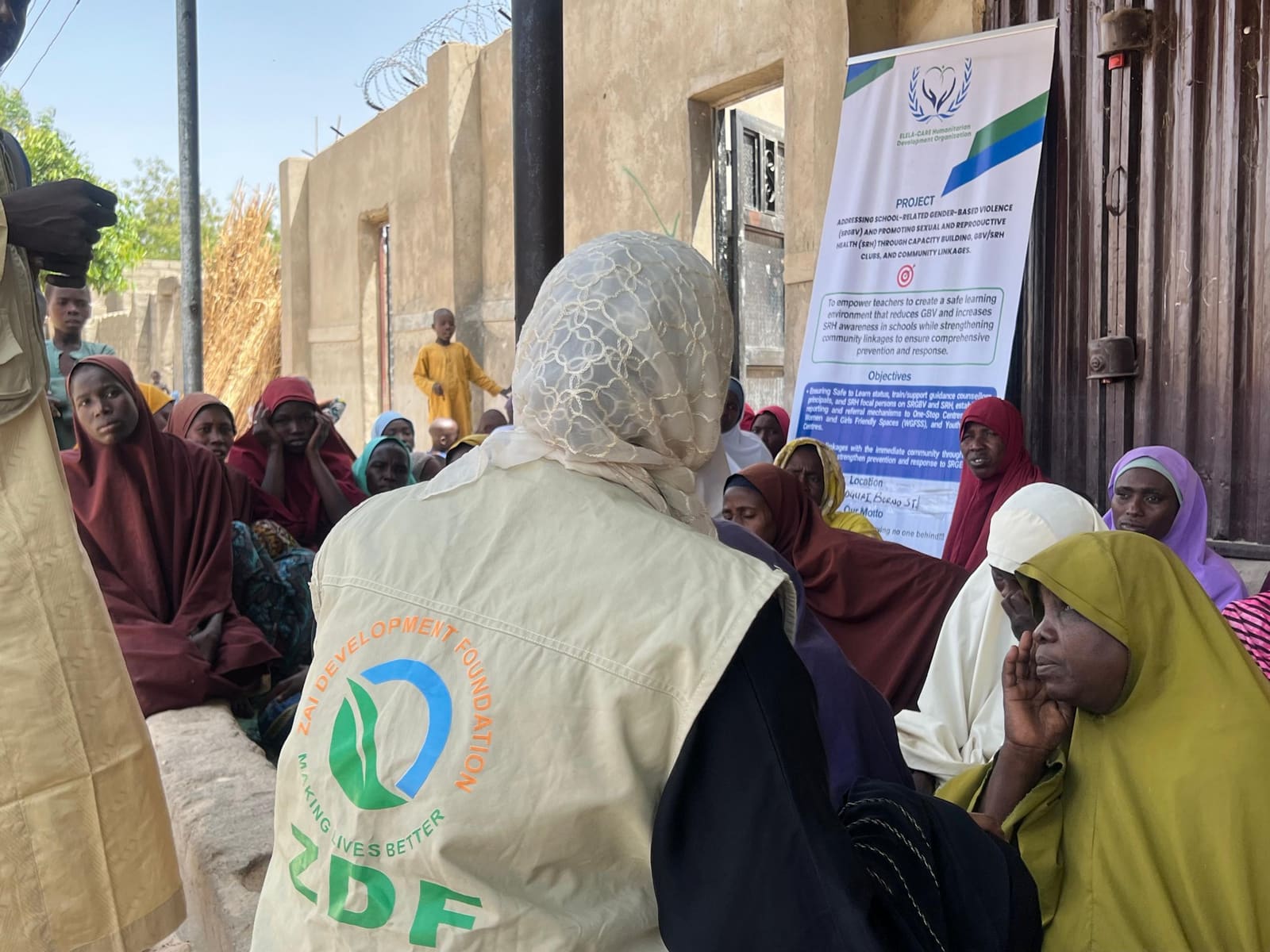 A ZAIDF team member in a ZDF vest speaks with seated women and girls