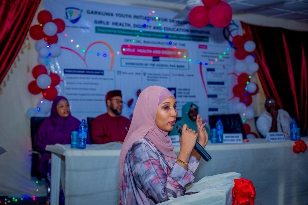 A facilitator addresses an audience in front of a decorated event backdrop